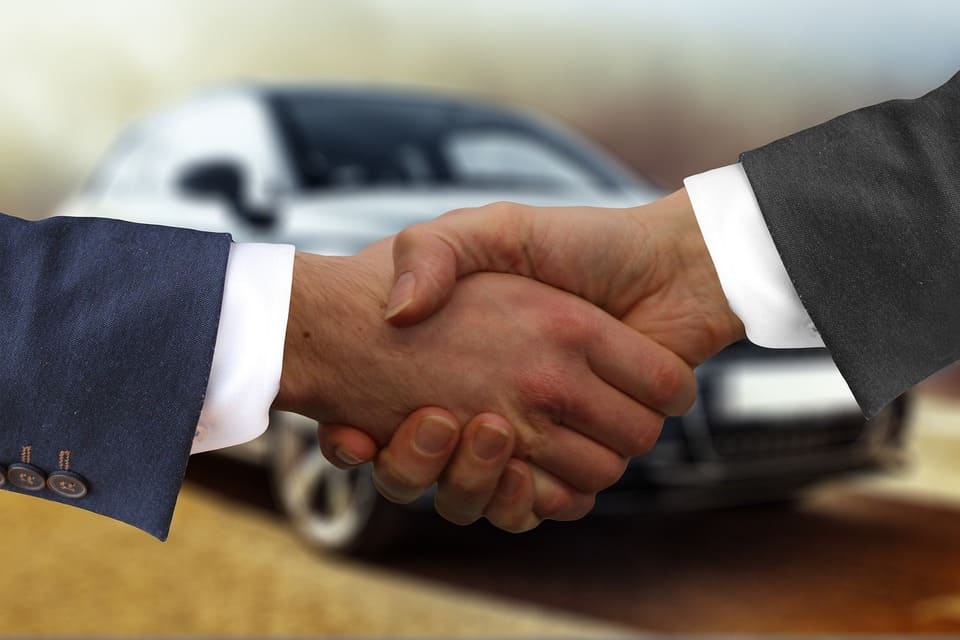 two-people-shaking-hands-in-front-of-a-vehicle