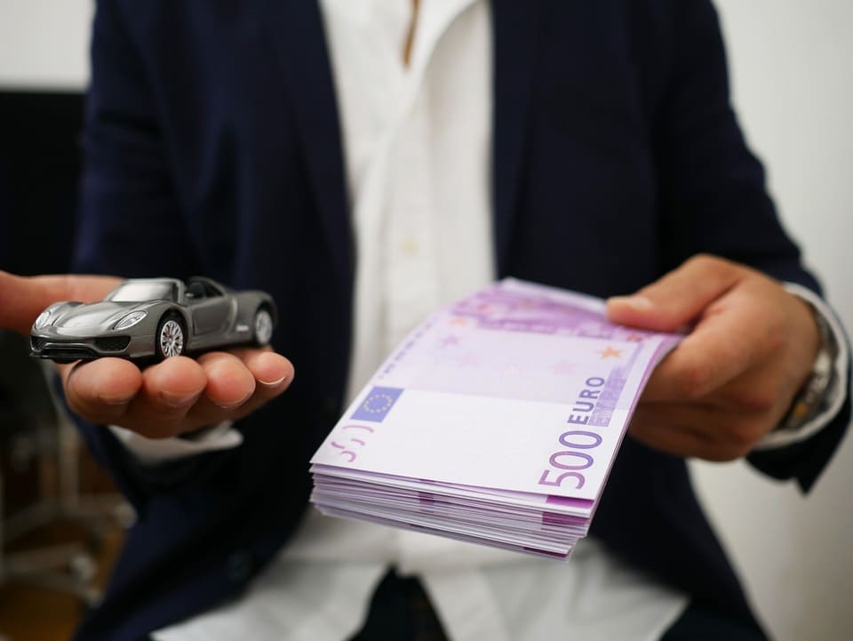 person-holding-out-a-car-figurine-and-a-stack-of-money