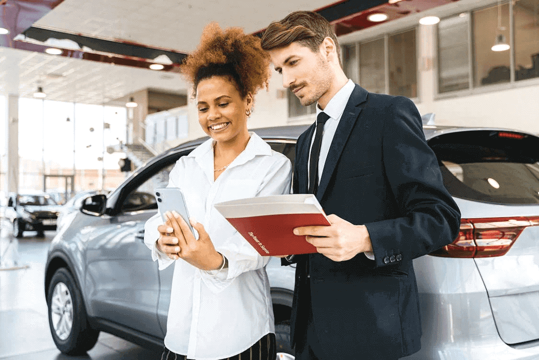 man-holding-a-form-standing-next-to-a-smiling-woman-in-front-of-a-car.png